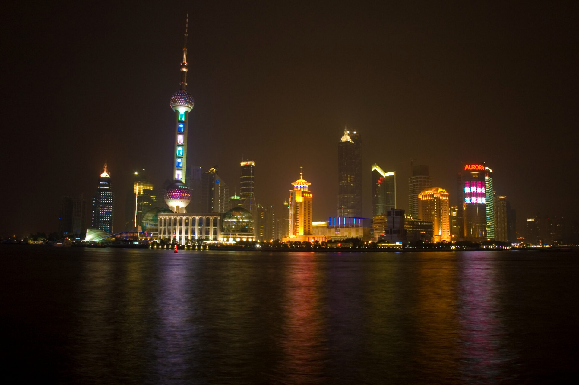 Beleuchtete Skyline von Shanghai bei Nacht mit dem Oriental Pearl Tower und Spiegelungen der Lichter auf dem Huangpu-Fluss.