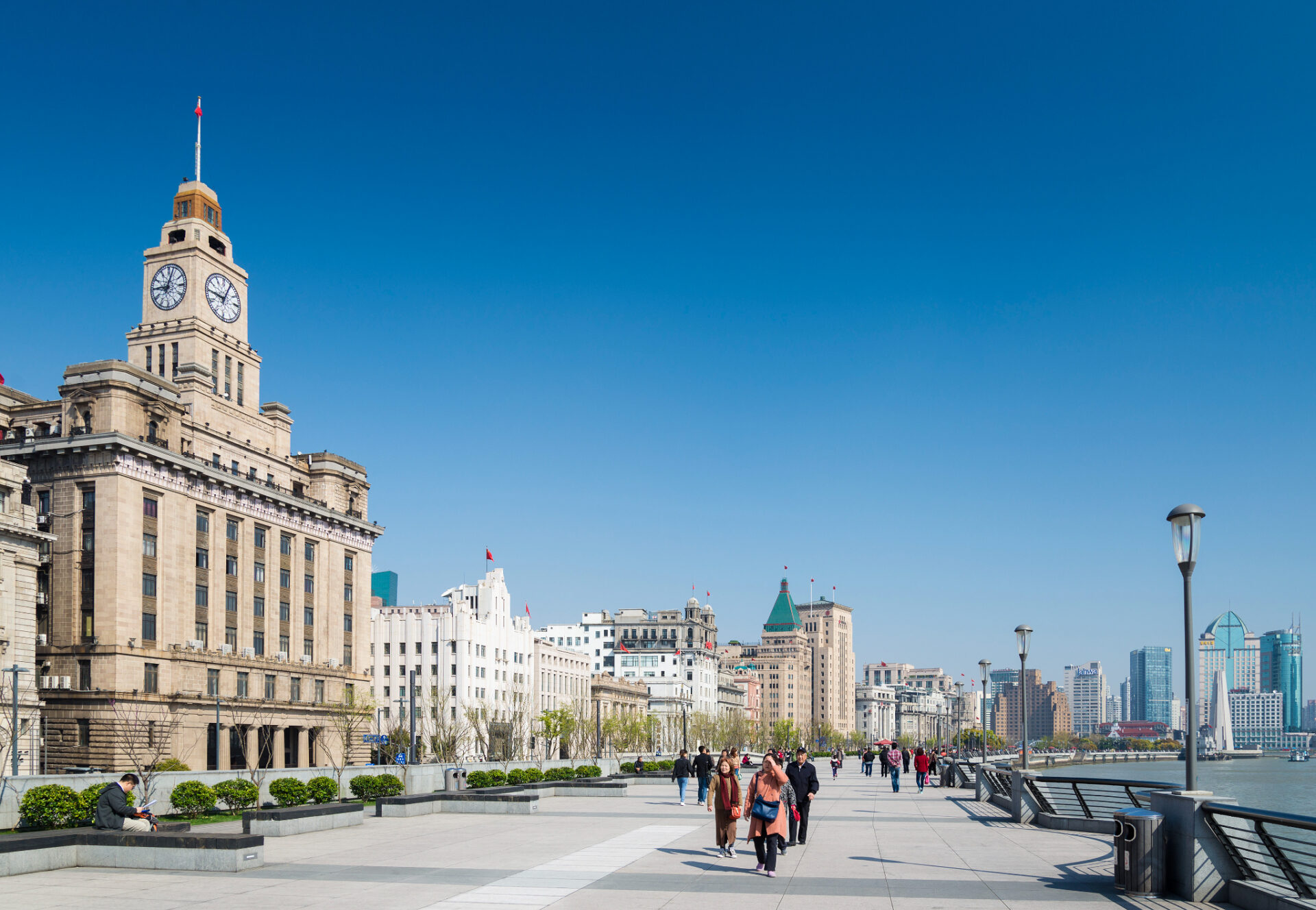 Promenade am Bund in Shanghai mit historischen Gebäuden, Spaziergängern und Blick auf den Huangpu-Fluss.